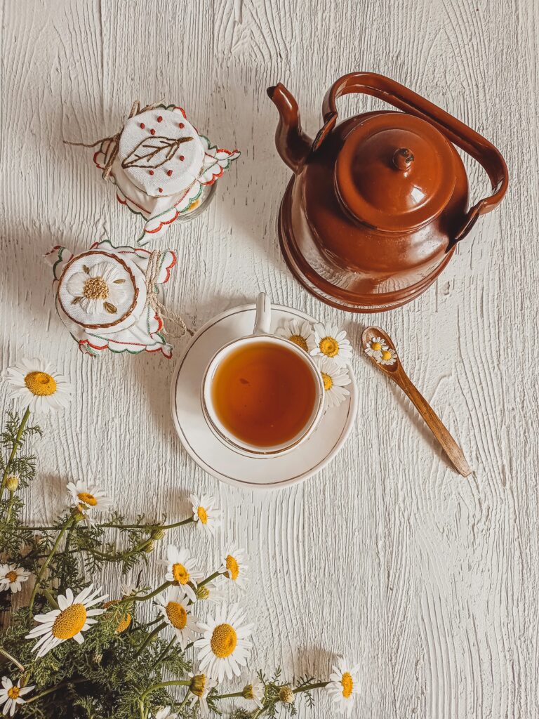 Top view of a ceramic tea set on wooden surface with chamomile flowers.